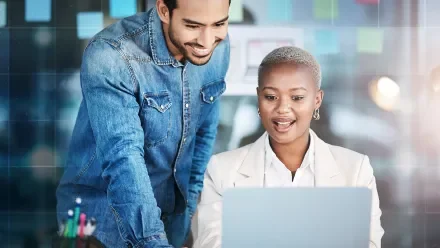 A man and woman in an office look at a laptop screen